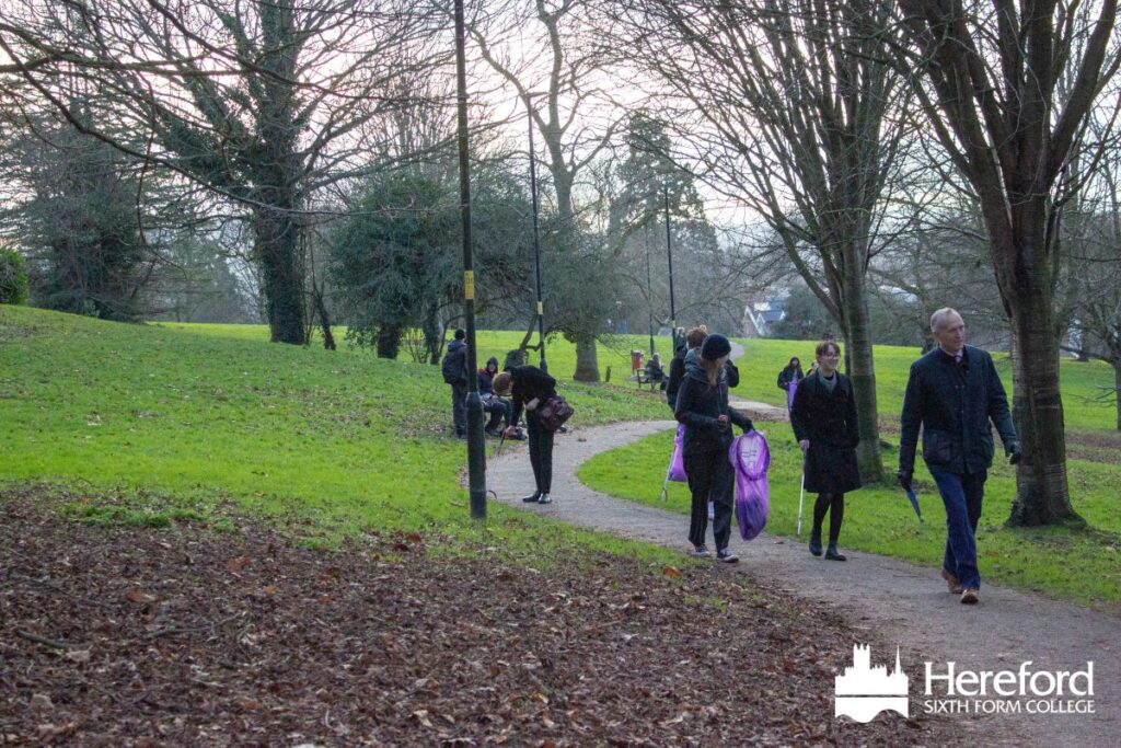 Photo of a park, a path winds into the distance. people walk on the path, several carry litterpicks or purple bags